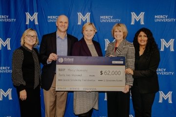 Oxford International Education Group and 鶹Ʒ officials pose in front of large cardboard check symbolic of the $62, 000 donation they made to the university